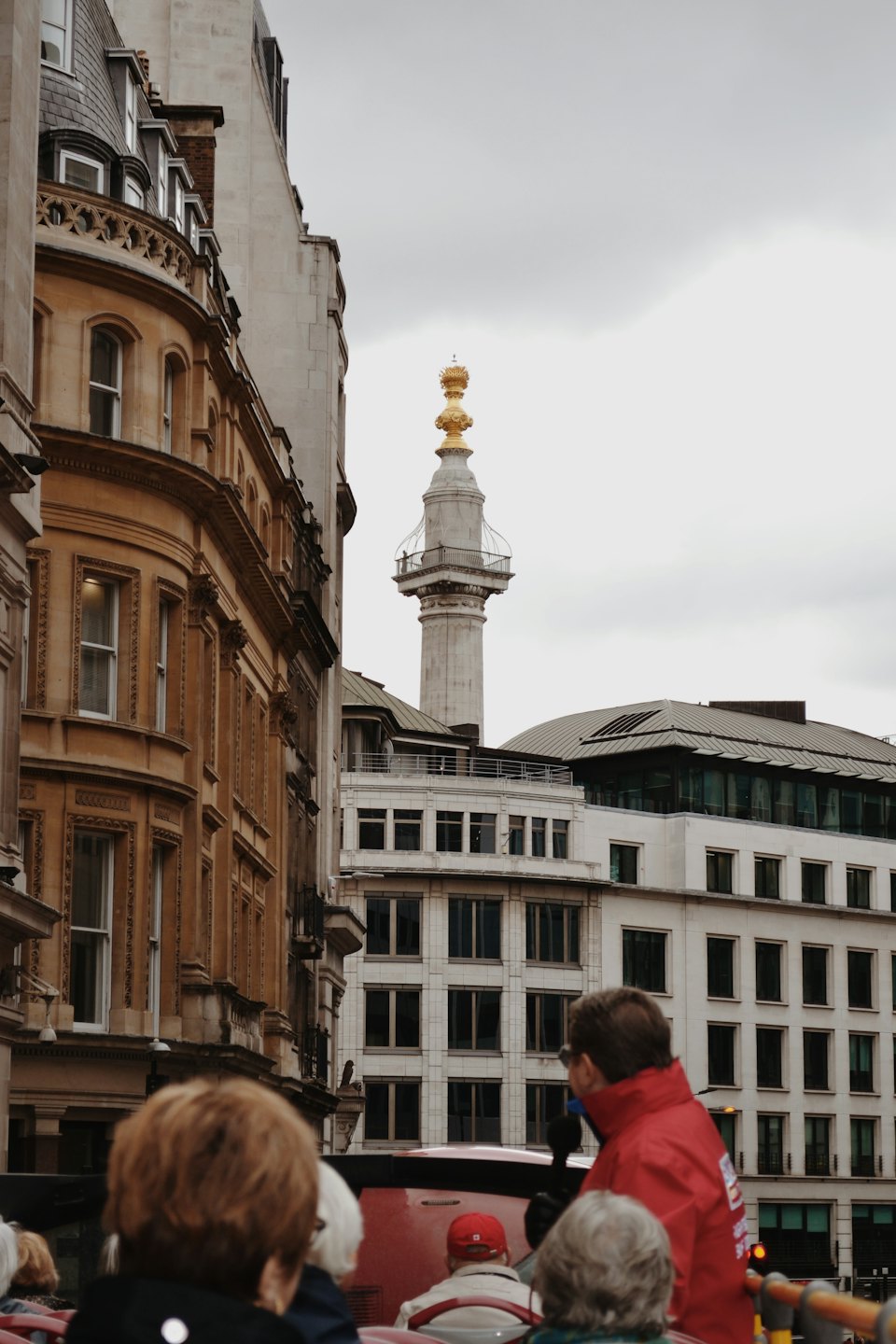 Tourists ride a double-decker bus past historical and modern city buildings.