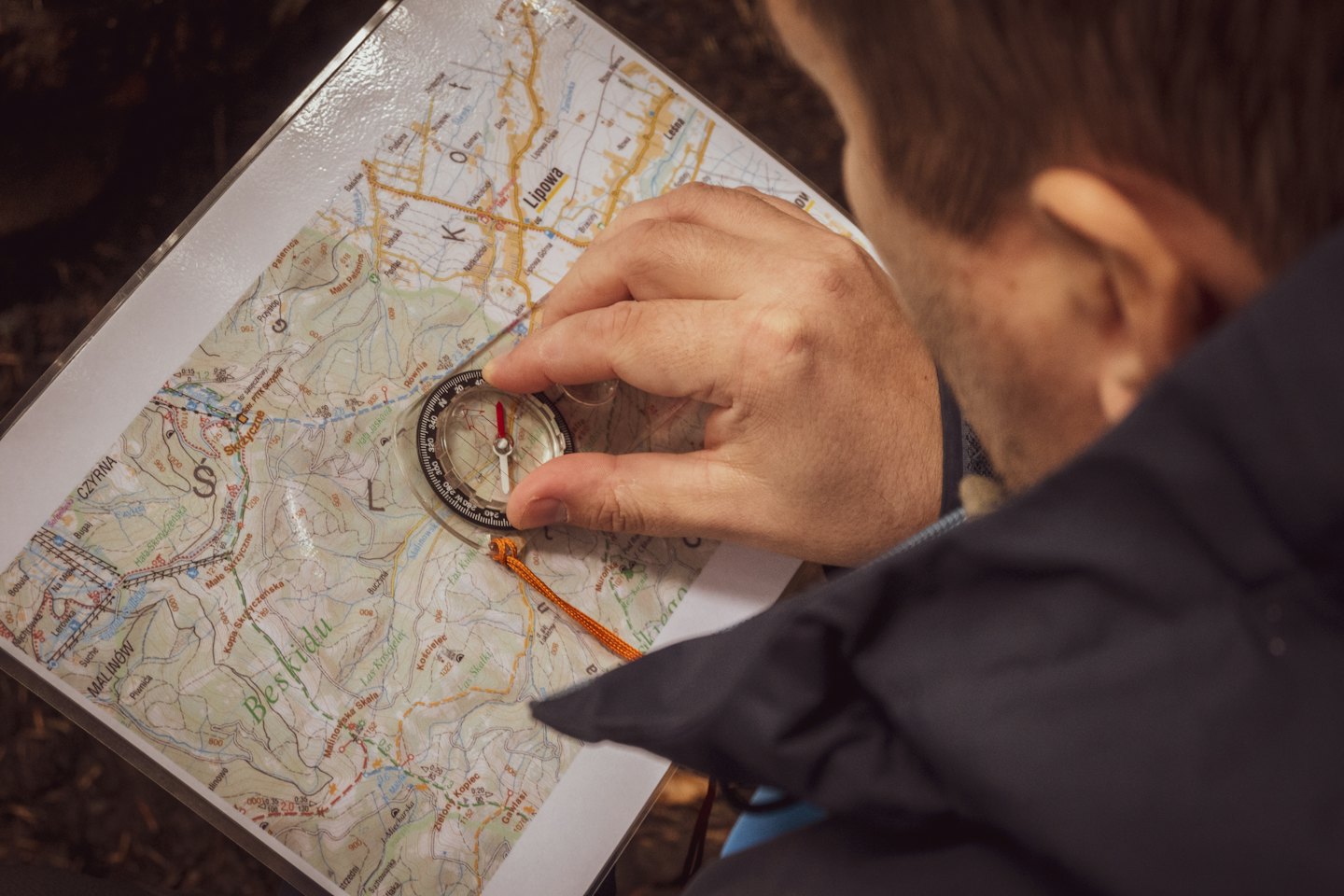 A person uses a compass to navigate a paper map.